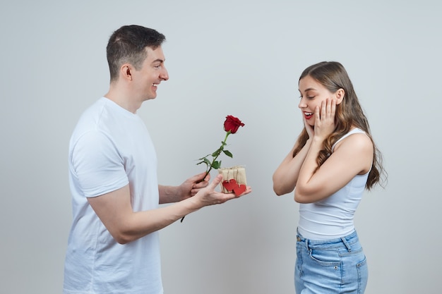 Een verliefde man geeft een verrast blondje een cadeau en een rode roos.