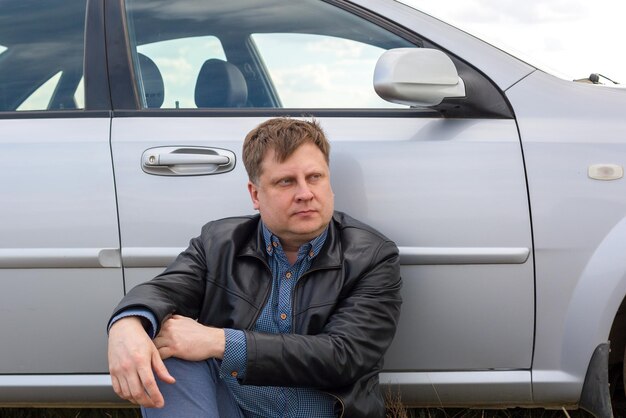 Foto een vermoeide chauffeur zit op het gras bij de auto in de steppe.