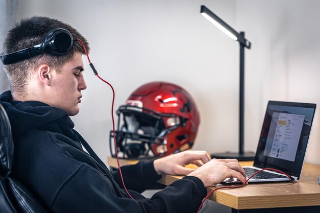 Een vermoeide tienerjongen met een koptelefoon zit voor een laptop in zijn kamer