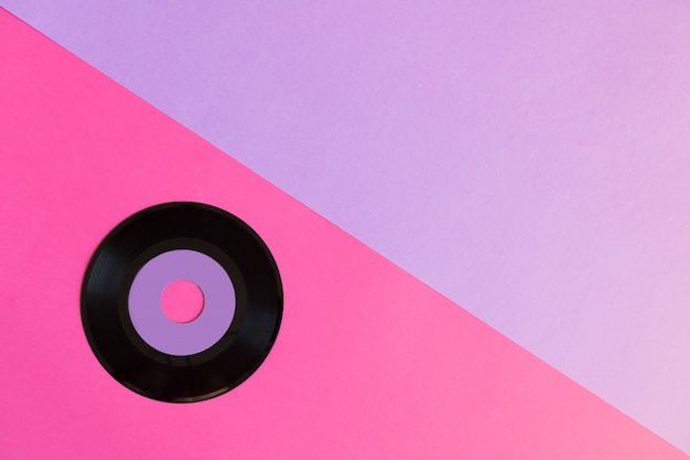 Een verouderde vinylschijf op een achtergrond van twee ton papier: roze en violet, popcultuur.