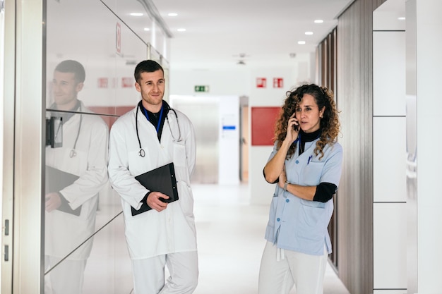 Een verpleegster aan de telefoon terwijl een arts de aantekeningen in een ziekenhuisgang doorleest