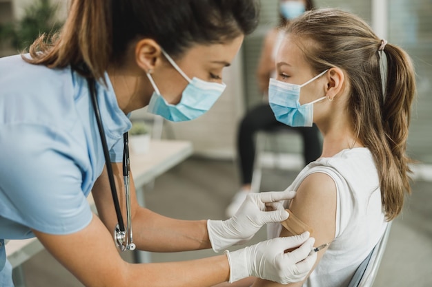 Een verpleegster die een pleister aanbrengt op een schattig tienermeisje na ontvangst van het Covid-19-vaccin.