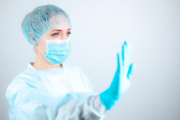 Een verpleegster in een doktersjas, masker en beschermende handschoenen staat zijwaarts met haar hand uitgestrekt in een "stop" -gebaar.