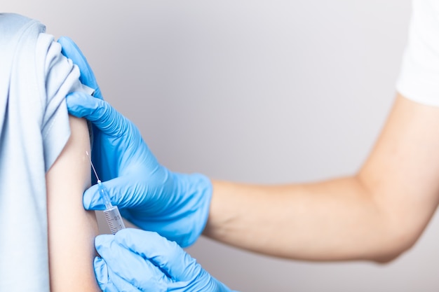 Een verpleegster met blauwe handschoenen injecteert een vaccin met een spuit in de schouder