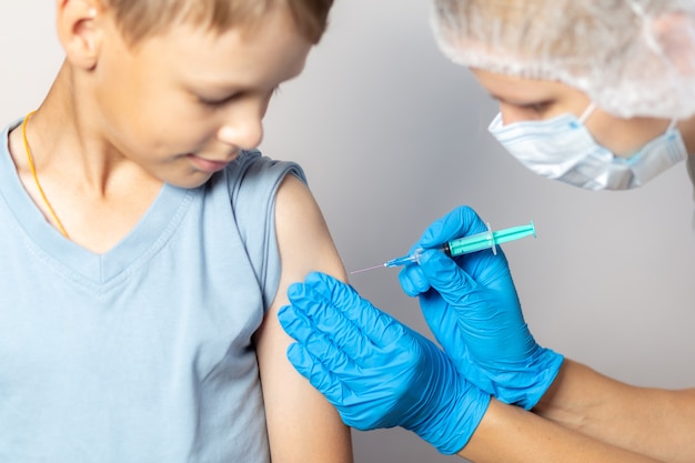 Een verpleegster met een masker en blauwe handschoenen injecteert het vaccin via een spuit in een jongen