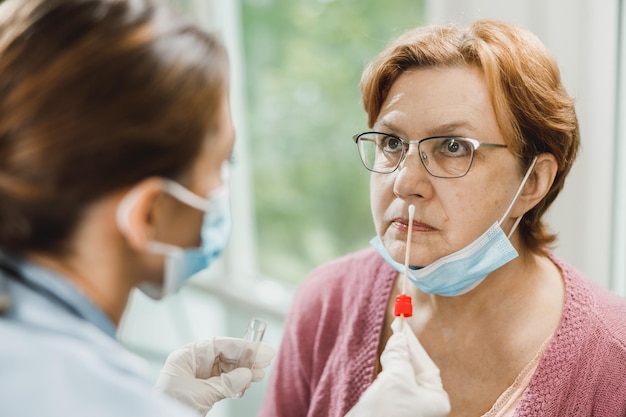 Een verpleegster neemt een monster uit de neus van een oudere vrouw voor een antigeentest op coronavirus.