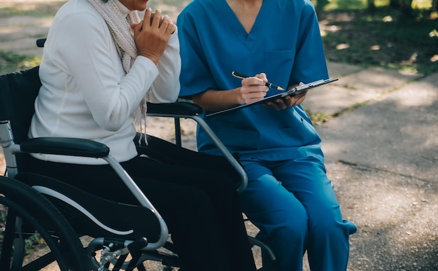 Een verpleegster zorgt thuis voor een oudere man in een rolstoel in zijn tuin