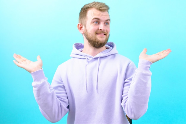 Een verraste man in een paarse hoodie spreidde zijn handen en de verbazing over de situatie met een blauwe achtergrond Frustratie Human Pose Verbaasd Verbaasd Wang Verwarring Expressief Gebaar