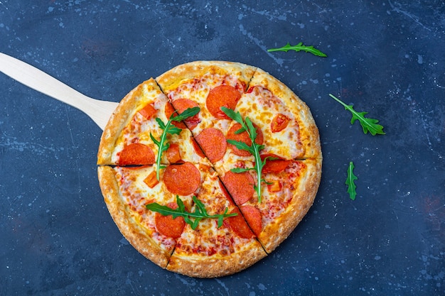 Een vers bereide pepperoni pizza met salami, tomaten en kaas op een donkere achtergrond. Italiaanse traditionele lunch of diner. Fast food en street food concept. Vlak ly, bovenaanzicht,