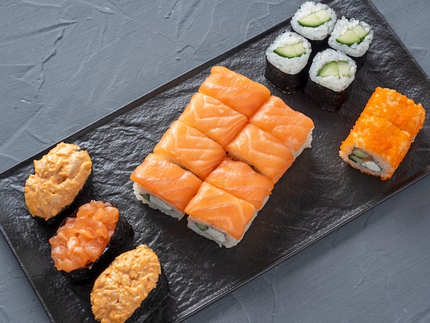 Een verscheidenheid aan broodjes en sushi gunkan genest op een zwarte plaat.