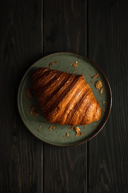 Een versgebakken heerlijke croissant op een bord op een houten tafel geschoten in donkere en humeurige stijl met natuurlijk licht van bovenaf selectieve focus