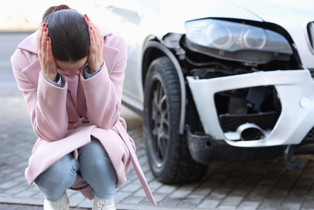 Een verstoorde vrouw zit met haar hoofd naar beneden naast een ontwikkelde auto