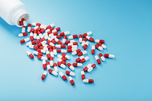 Een verstrooiing van rode en witte tablettencapsules uit een witte pot op een blauwe achtergrond. Geneesmiddelen, medicijnen, vitamines