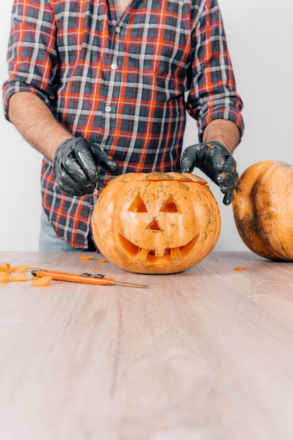 Een verticale opname van een persoon die handschoenen draagt en een pompoen voor Halloween uitsnijdt
