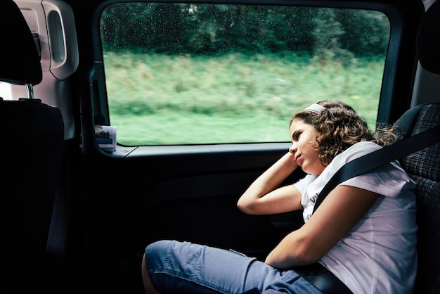 Een verveeld meisje dat door het raam kijkt terwijl het in de auto zit.