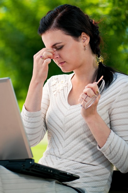Een verveelde jonge vrouw die met een laptop werkt in het zomerpark een stressvolle zakenvrouw buiten