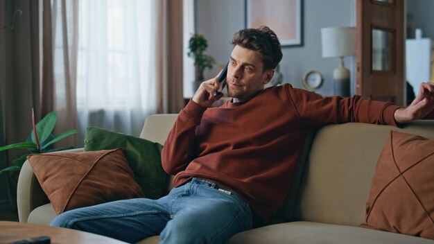 Foto een verveelde man die aan het bellen is, ontspant zich op de bank, een serieuze man die over een smartphone praat.