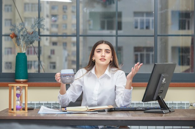 Een verward meisje dat achter het bureau zit en een kopje thee vasthoudt