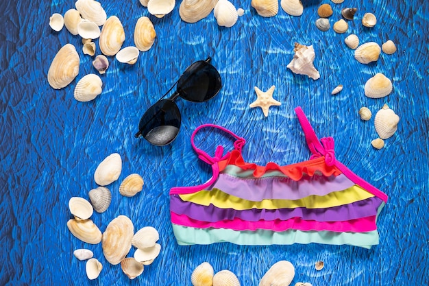 Een verzameling reisartikelen, waaronder een koffer, zonnebril, zwempak, zonnebrandcrème en schelpen op een turquoise marineblauwe achtergrond
