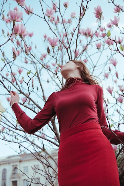 Een vetharig meisje in het rood tegen de achtergrond van een magnoliaboom het concept van eenheid met de natuur