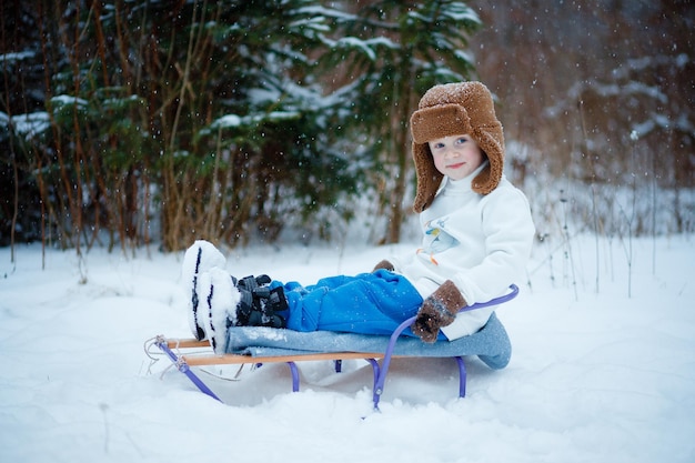 Foto een vierjarige jongen zit op een slee in een besneeuwd bos het sneeuwt zwaar