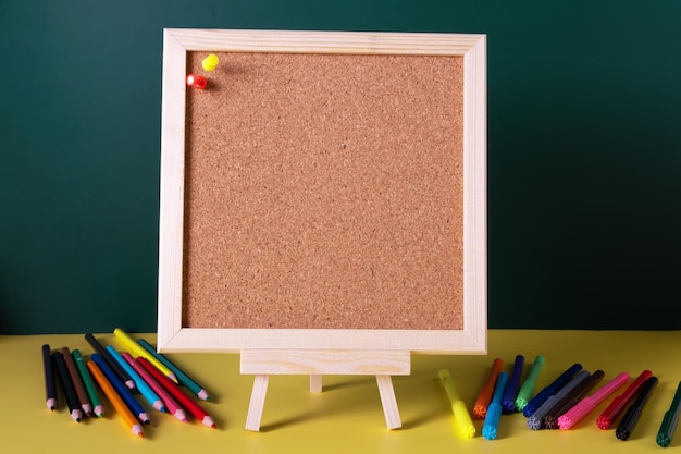 Foto een vierkant kurken notitiebord staat op een gele tafel met kleurpotloden en stiften ernaast