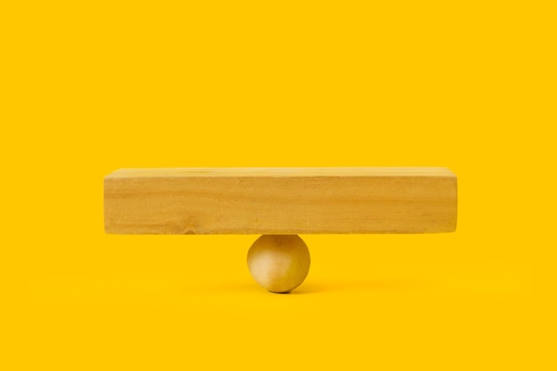 Een vierkante houten voet op een houten bal en op een gele ondergrond