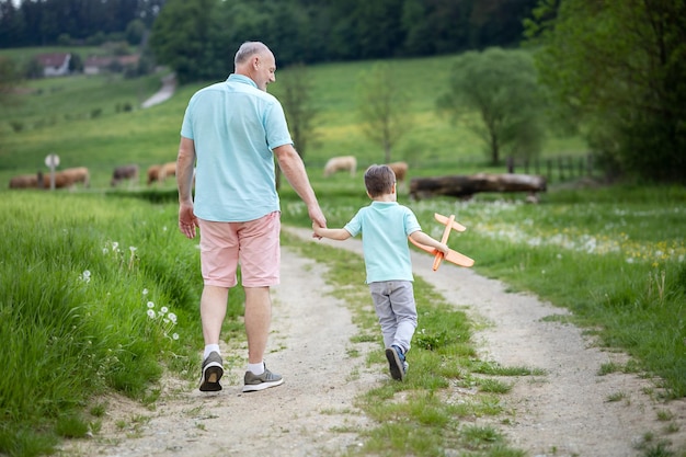 Een vijfjarige jongen loopt met zijn grootvader op een landelijke weg en ze praten