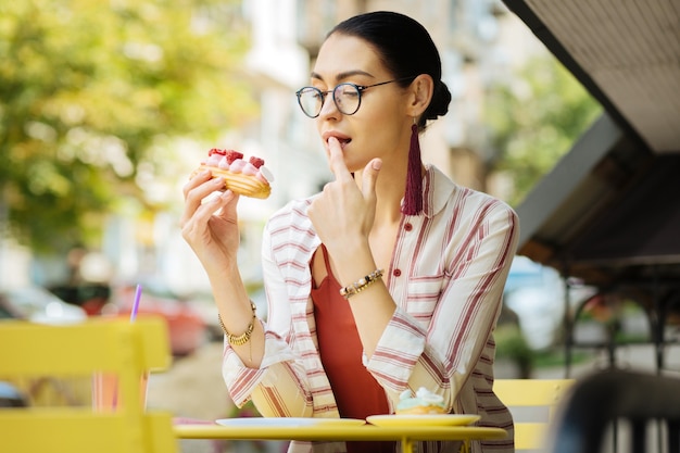 Een vinger likken. Jonge vrouw voelt zich onder de indruk en likt haar vinger tijdens het eten van heerlijke frambozen eclair in een café