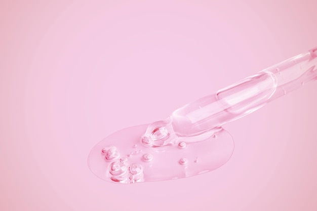 Een vloeiende heldere gel uit een pipet Veel vloeiende gel in een grote druppel met bubbels op een roze achtergrond