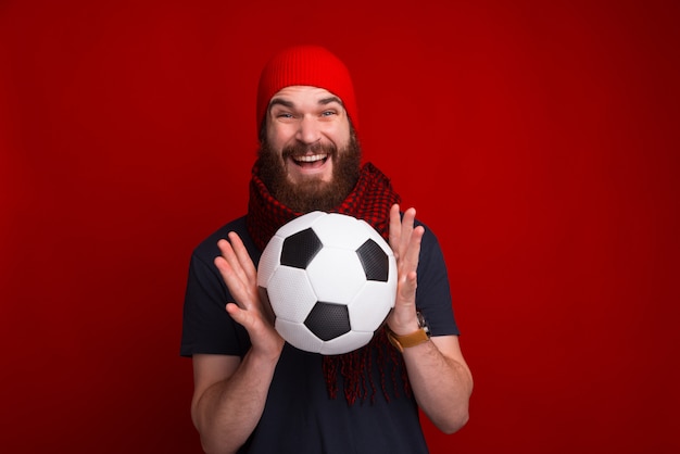 Een voetbalsupporter die warme kleren draagt en een voetbalbal over rode ruimte colding