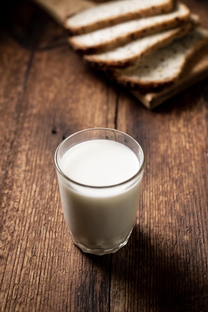 Een vol glas melk Brood op de achtergrond is wazig Donkere houten achtergrond Ochtendontbijt Gezonde voeding Verticaal frame