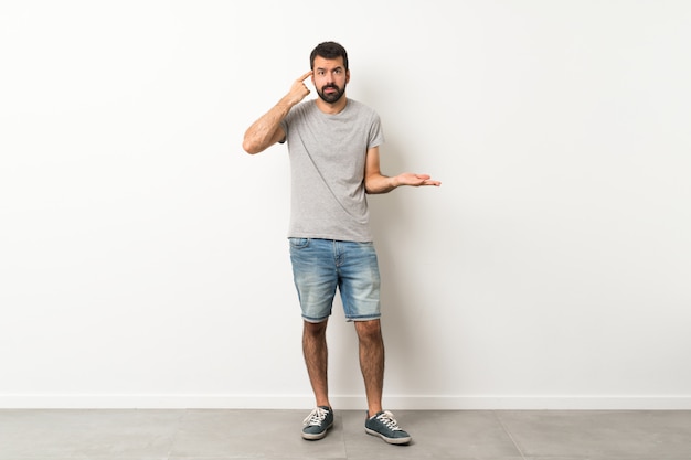 Een volledig schot van de knappe man met baard die het gebaar van waanzin maakt die vinger op het hoofd zet