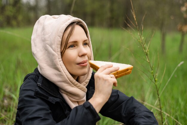 Een volwassen aantrekkelijke vrouw eet een broodje buiten in het bos, park. Snack op een wandeling, op een wandeling.