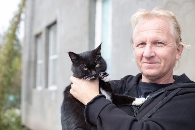 Foto een volwassen blonde man houdt een grote zwarte kat in zijn armen. liefde voor huisdieren.