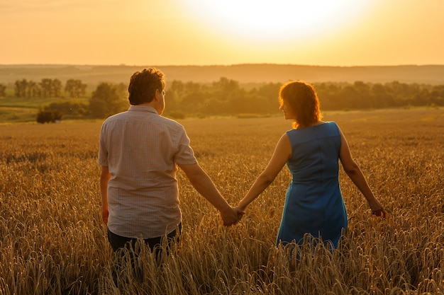 Een volwassen boer en zijn vrouw lopen hand in hand door hun tarweveld.