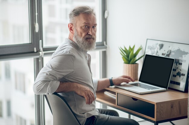 Een volwassen man in een wit t-shirt die op een laptop werkt