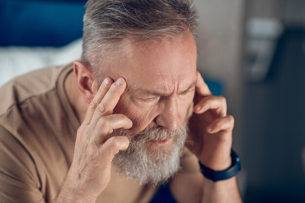 Een volwassen man met een baard die hoofdpijn heeft