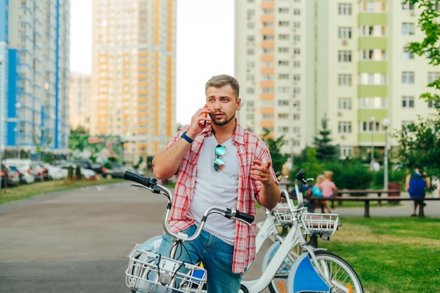 Een volwassen man met een gehuurde stadsfiets staat op straat en praat aan de telefoon tegen de achtergrond van de microdistricttuin een man op een fiets belt aan de telefoon