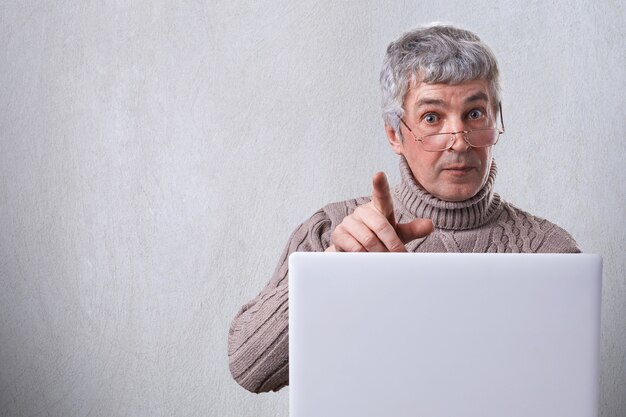 Een volwassen man met grijze haren dragen van een bril aan de tafel werken met zijn laptop