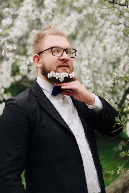 Een volwassen man met witte bloemen in zijn baard tegen een achtergrond van lentekersenbloesems 1