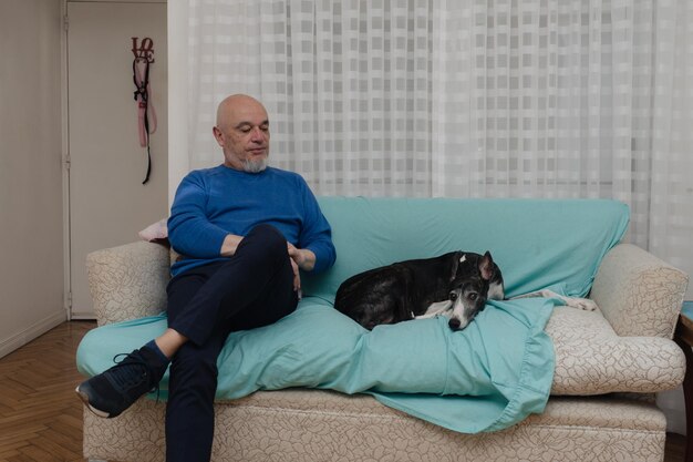 Een volwassen man met zijn windhond die thuis op de bank zit.