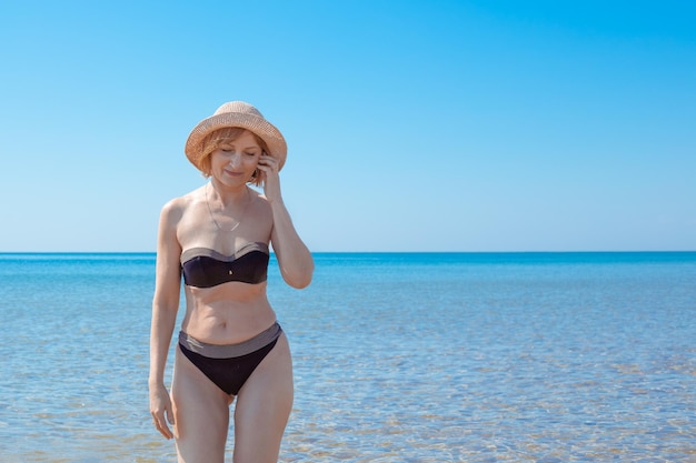 Een volwassen slanke vrouw in een zwempak loopt langs de kust op een zonnige zomerdag Vakantie op zee