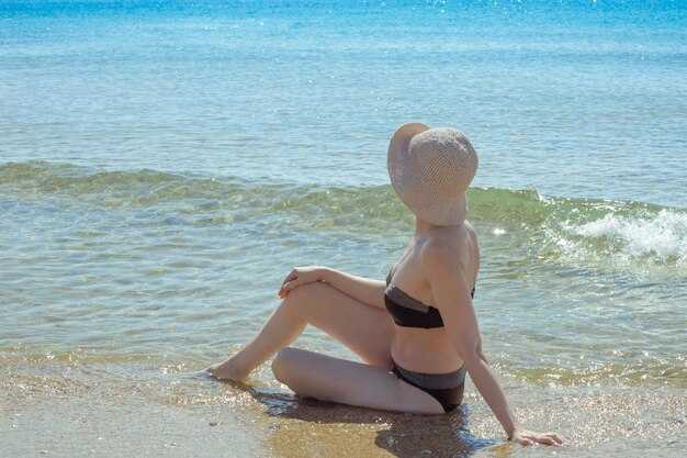 Een volwassen slanke vrouw in een zwempak zit in zeewater en kijkt naar de zee Zomervakantie rust en ontspanning