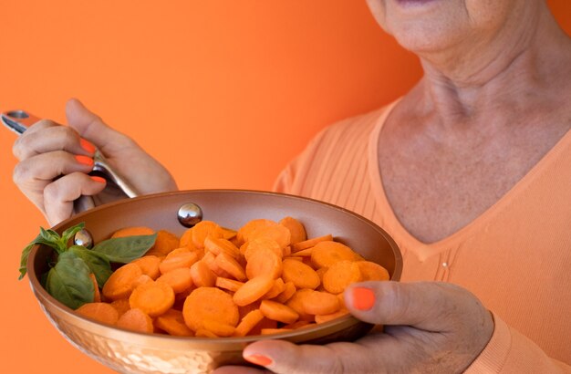 Een volwassen vrouw houdt een pan vol ronde gesneden wortelen omhoog Dieet gezond plantaardig veganistisch concept