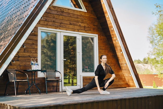 Een volwassen vrouw in activewear sport op het terras van de blokhut