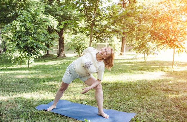 Een volwassen vrouw in een T-shirt doet fitnessoefeningen en doet yoga buitenshuis, een gezonde levensstijl