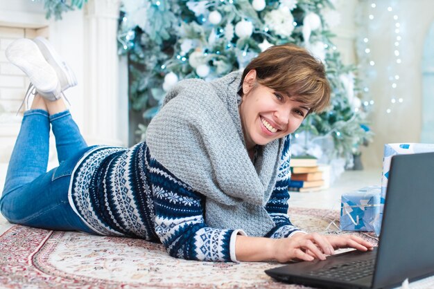Een volwassen vrouw ligt met een laptop in de buurt van een kerstboom