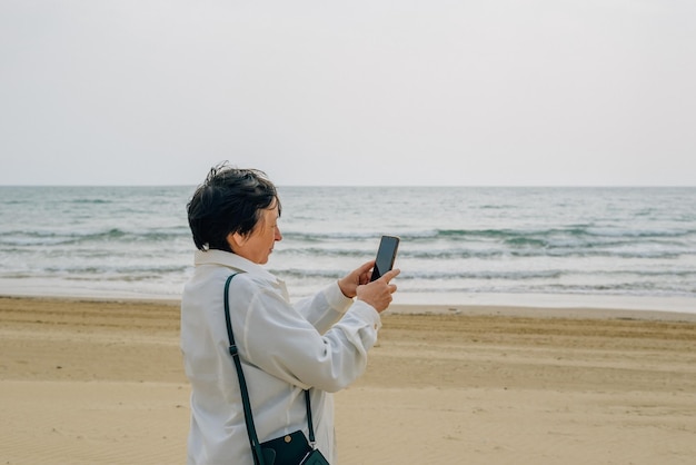 Een volwassen vrouw op het strand bij de oceaan in de lente tijdens een picknick maakt een selfie en praat een video