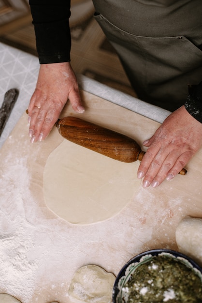 Een volwassen vrouw rolt deeg in haar keuken om bakken of knoedels, manti voor te bereiden